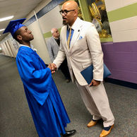 A graduate in blue cap and gown shaking hands with a man.