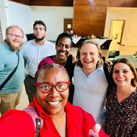 A group of smiling colleagues posing for a selfie in an indoor setting.