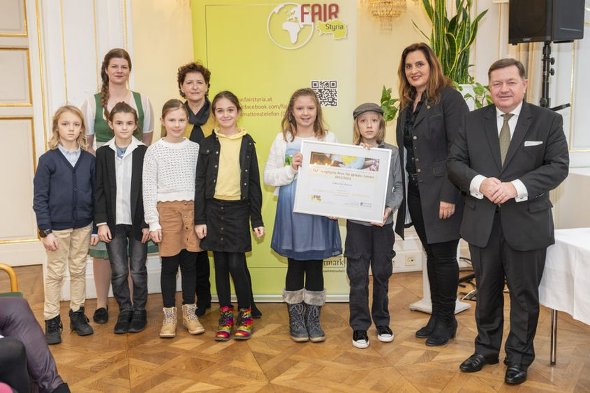 Kindergruppe hält Preisurkunde, FAIR, mit Personen, Volksschule Retznei im Hintergrund.