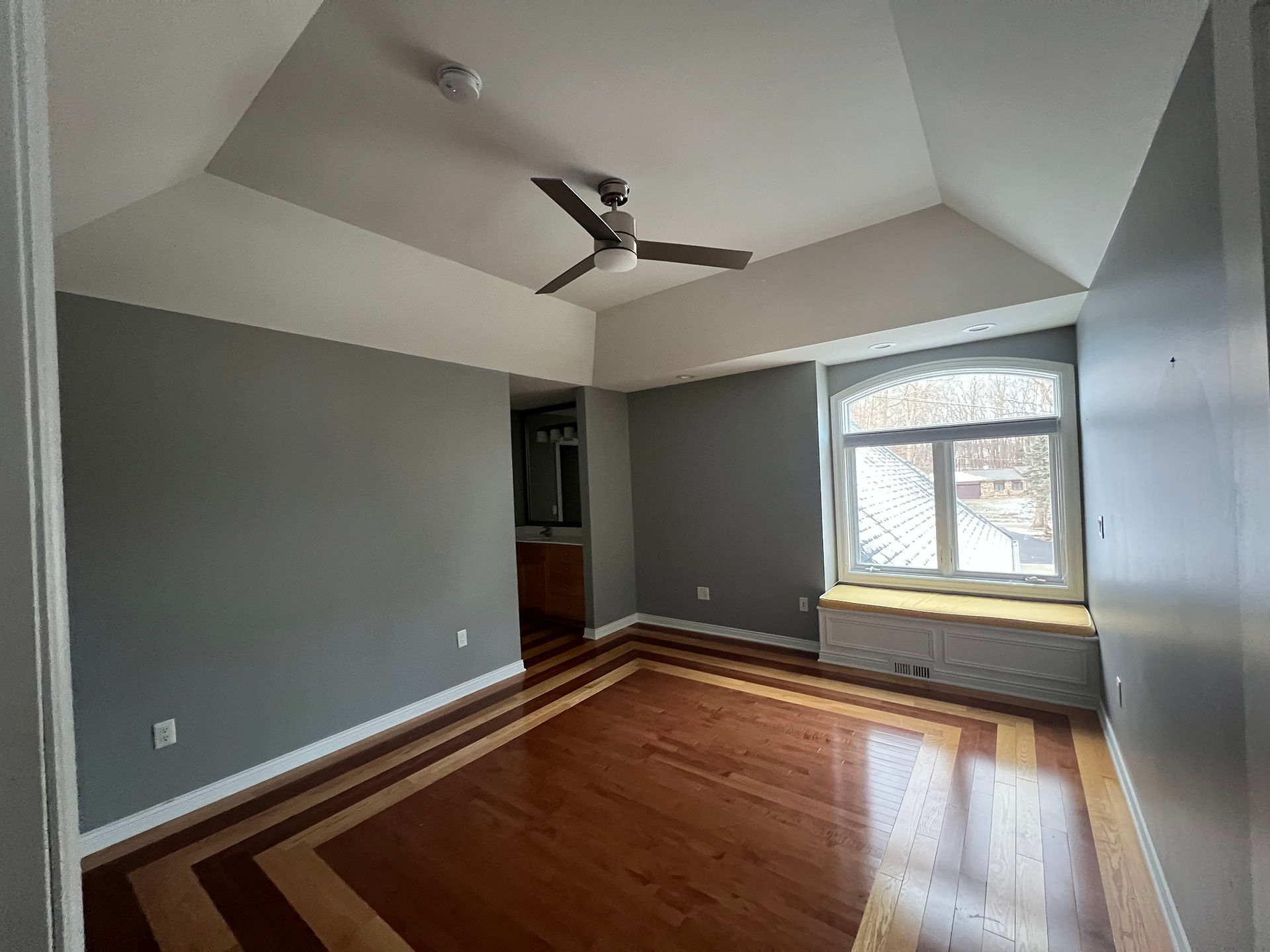 An empty bedroom with blue walls, a ceiling fan, and wood floors