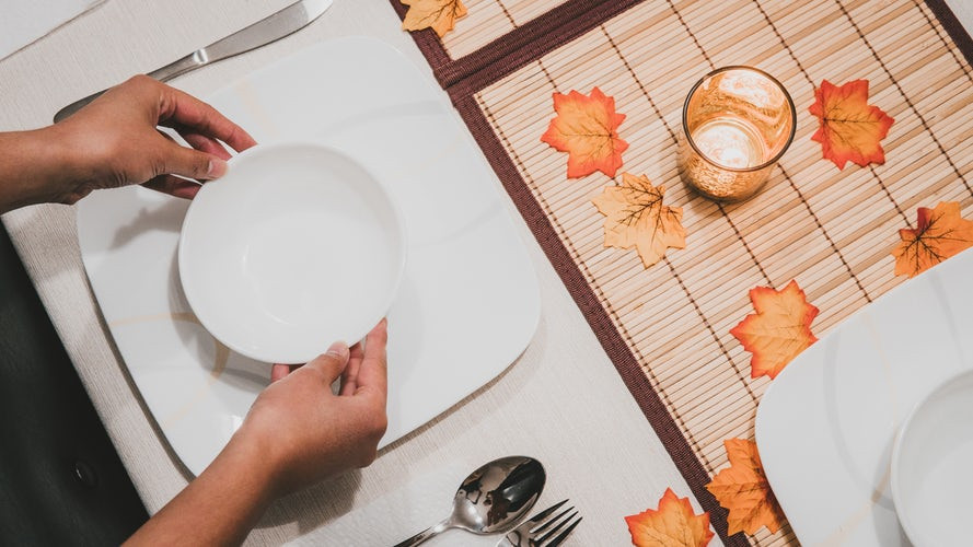 A person arranging dinnerware on a table for Thanksgiving.