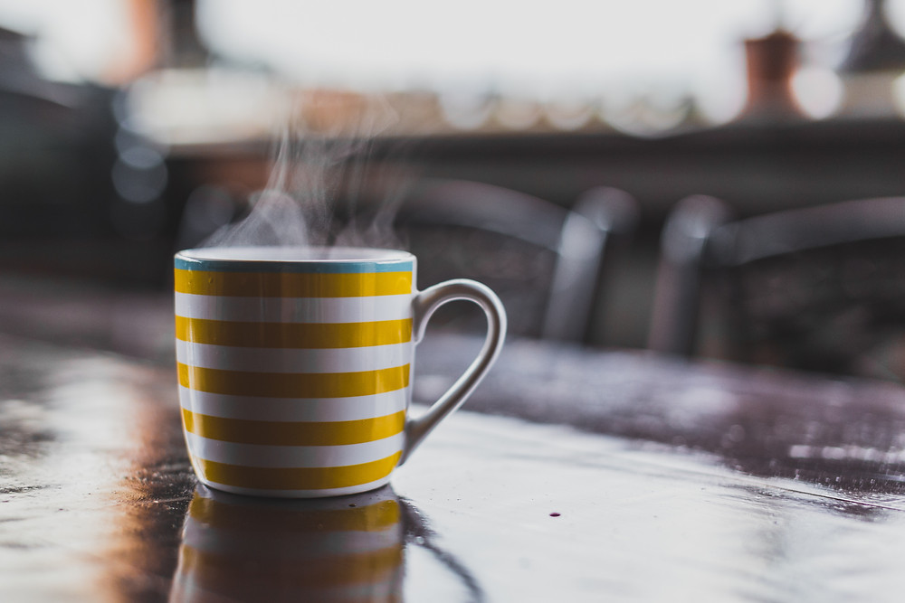 A steaming hot toddy in a yellow and white striped mug.