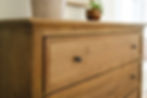 Wooden dresser with black knobs, topped by two potted plants. Bright, minimalistic room. Warm natural tones create a cozy atmosphere.