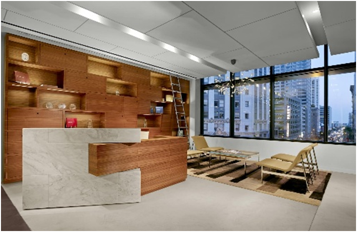 Modern office with wooden shelves, marble reception desk, glass windows showing cityscape. Neutral chairs on a patterned rug, ladder nearby.