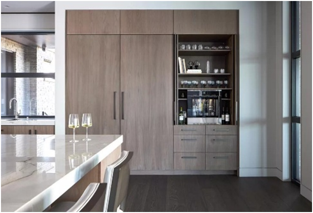 Modern kitchen with a marble island, wood cabinets, glassware displayed, and three filled wine glasses. Bright and elegant setting.
