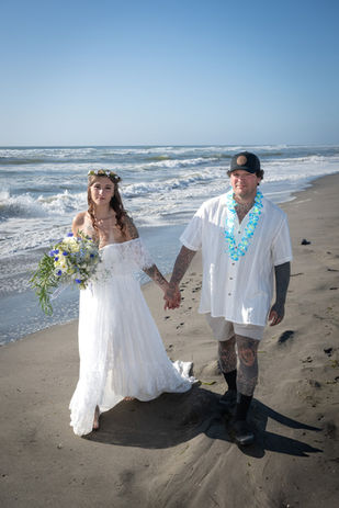 Newlywed couple walking along the beach in Long Beach, Washington, with the bride carrying a custom blue and white wedding bouquet.