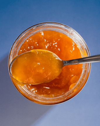 A view of a glass of apricot jam from above, spoon full of jam resting on the open top of the glass.