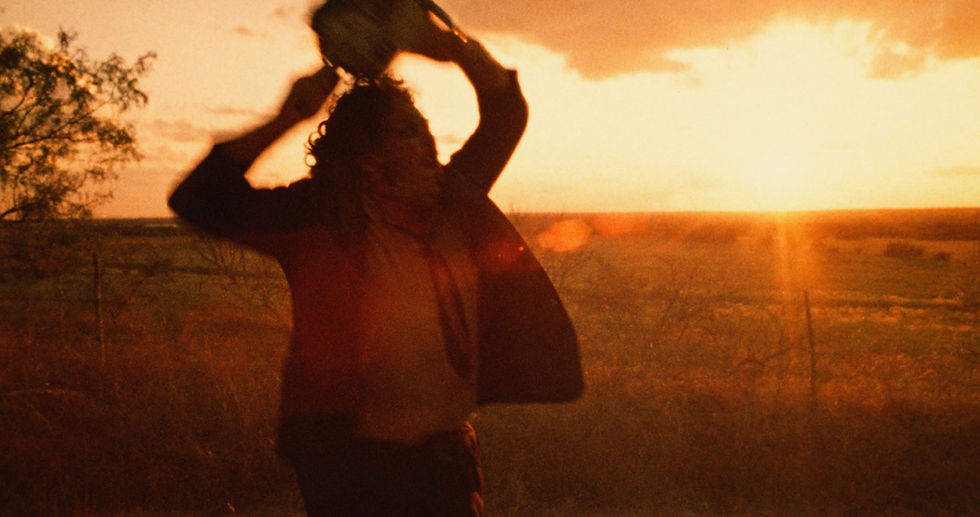 Silhouetted figure swings chainsaw in sunset field, creating dramatic and intense scene. Orange hues fill the sky, adding tension.