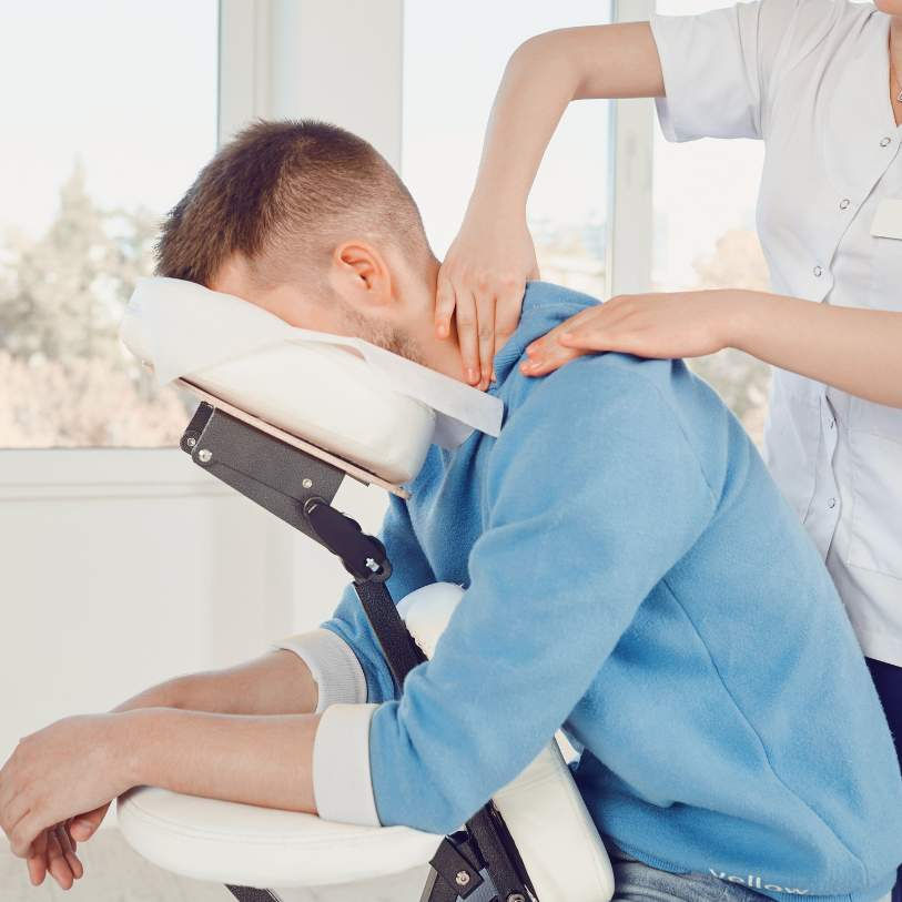 "Person receiving a seated neck and shoulder massage from a professional massage therapist in a bright, airy room."