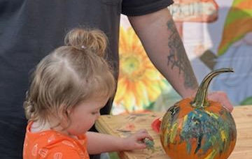 A toddler sitting on a stool painting a pumpkin at Buffalo Moon Fall Artisan Market at Lakota's Farm.