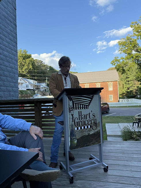 Author reading outdoors behind a podium that reads "Hart's Grocery"