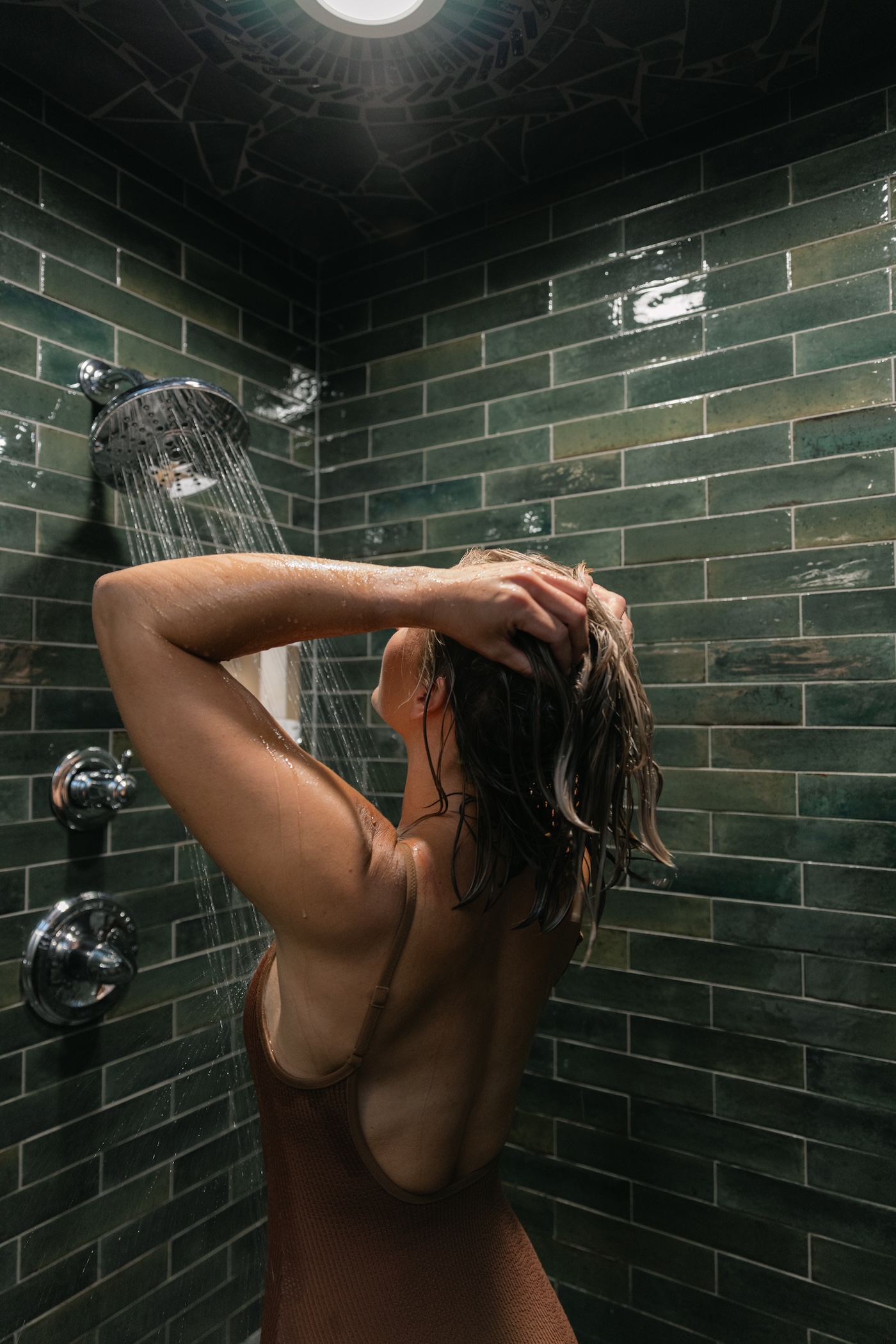 Guest rinsing her hair in the green-tiled plunge suite shower
