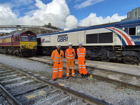 people in high visibility clothing and PPE standing between tracks at a quarry railway terminal with two diesel locomotives in the background