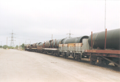 train of flatbed wagons with large pipes on in railway yard