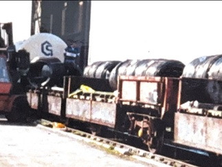forklift truck loading coils of steel onto wagons which are on rail