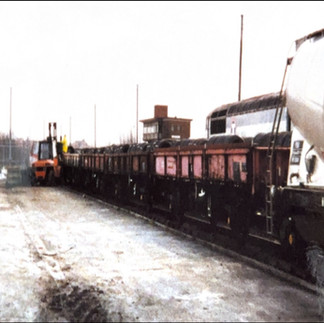 railway wagons on a track with locomotive in the background and forklift truck alongside the train