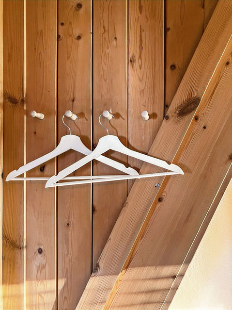 white coat hangers on pegs on a vertical shiplap wooden wall