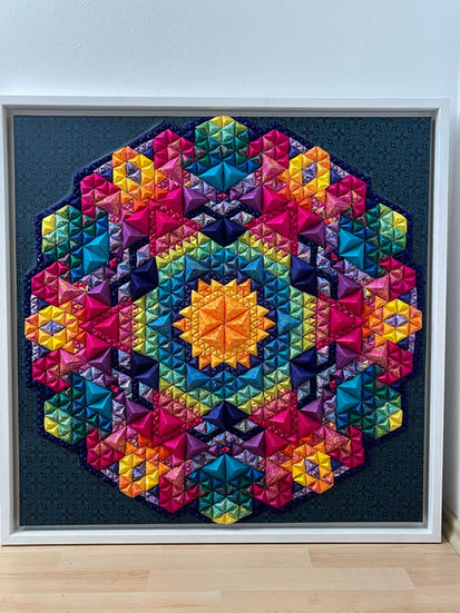 a colorful quilt in a white frame on a wall