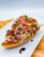 Toast topped with colorful diced vegetables and balsamic glaze on a white plate. The background is a wooden texture.