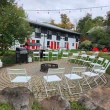 Outdoor patio with fire pit, chairs, and white building with red doors