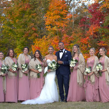 Bride, groom, and bridesmaids in pink dresses, autumn trees.
