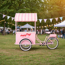 "A pastel pink ice cream tricycle cart with a striped canopy and 'Happy Day!' written on the side, parked on a grassy field w