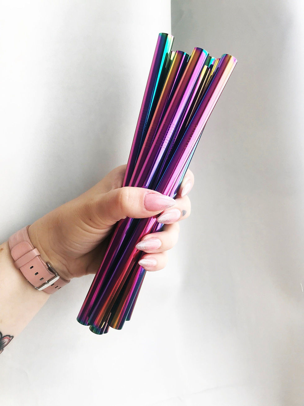 A hand with long beige nails holding a bunch of chrome metallic straws