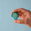 Thumbnail: Bumbu Toys Green Seashell held between thumb and forefinger, showing its size and curved shape