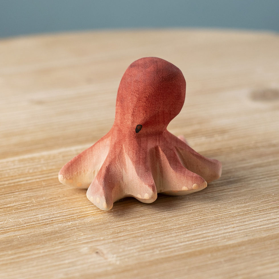 Bumbu Toys Wooden Octopus on a wooden surface, showing its soft curves and gradient coral colouring