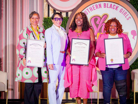 Four women smiling, holding certificates in front of a "Southern Black Girls" sign. Background features pink and green decor.