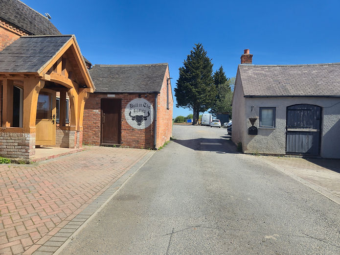 Path between rural buildings, one with a timber porch, one with a bull painting