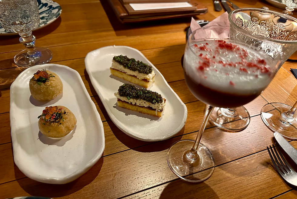 Elegant dining scene with two plates of gourmet appetizers and a cocktail. Wooden table, intricate glassware, and an inviting ambience. Caviar tops one