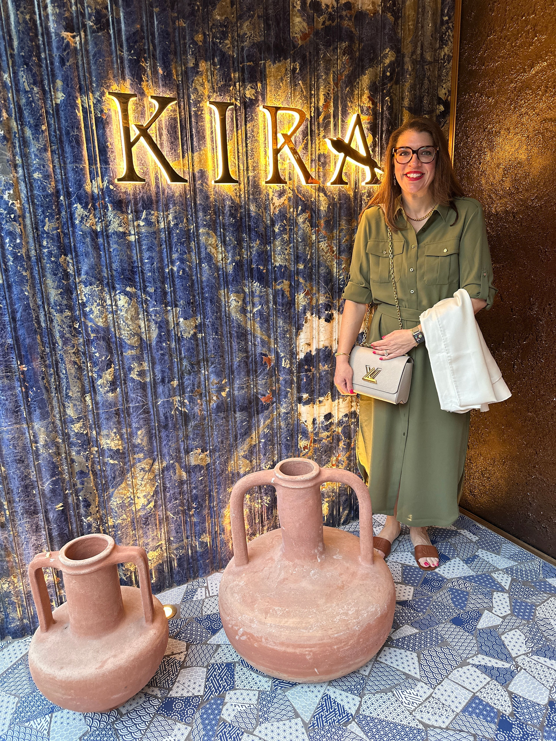 Kira posing with Kira sign in front of Gold light up luxury sign. Blue pattern curtain and pink jugs. Luxury decor and stunning location.