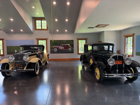 Wide view of a private automobile garage with a hand-painted Duesenberg mural and collector cars in the foreground