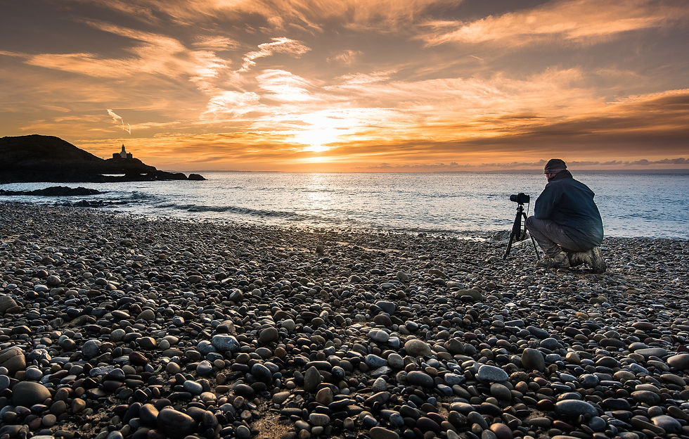 Sunset over a pebbly beach with a photographer in the foreground