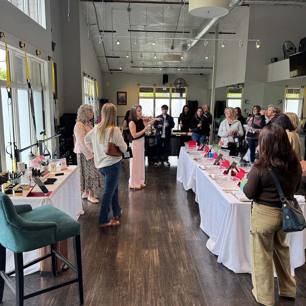 A woman speaks to a group in a bright room with tables displaying products. Attendees listen attentively, creating a focused atmosphere.