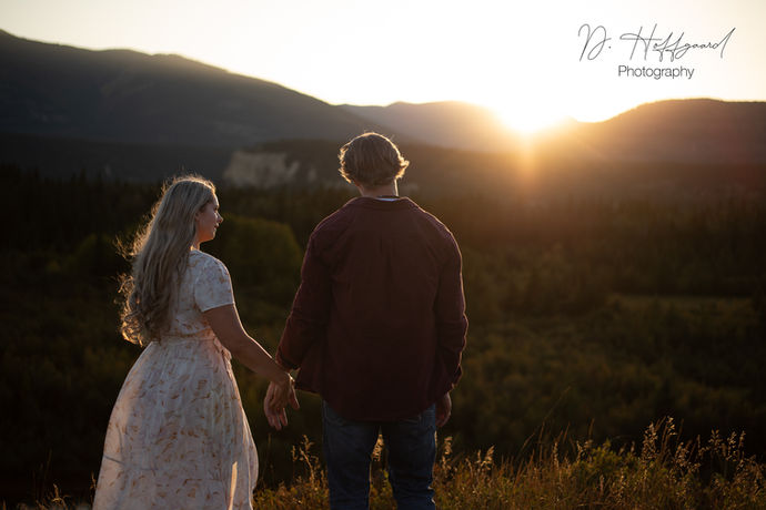 A woman in a white dress holding her fiancés hand while embracing a mountain sunset in Fairmont