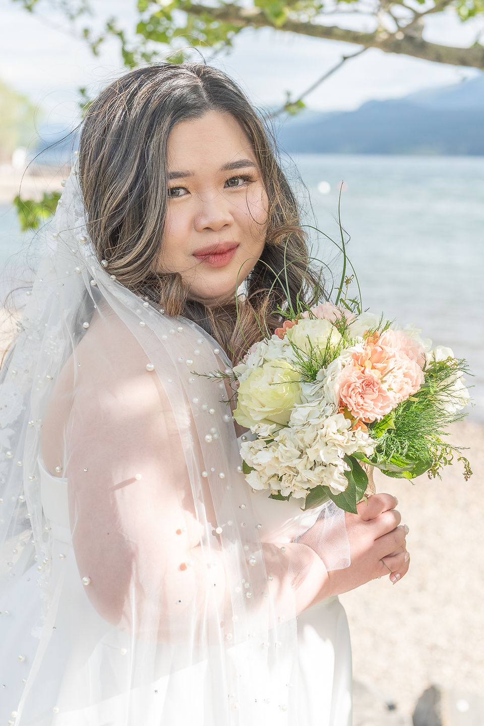 Elegant portrait of the bride holding her bouquet in front of the lake, a perfect spring wedding moment in Invermere.