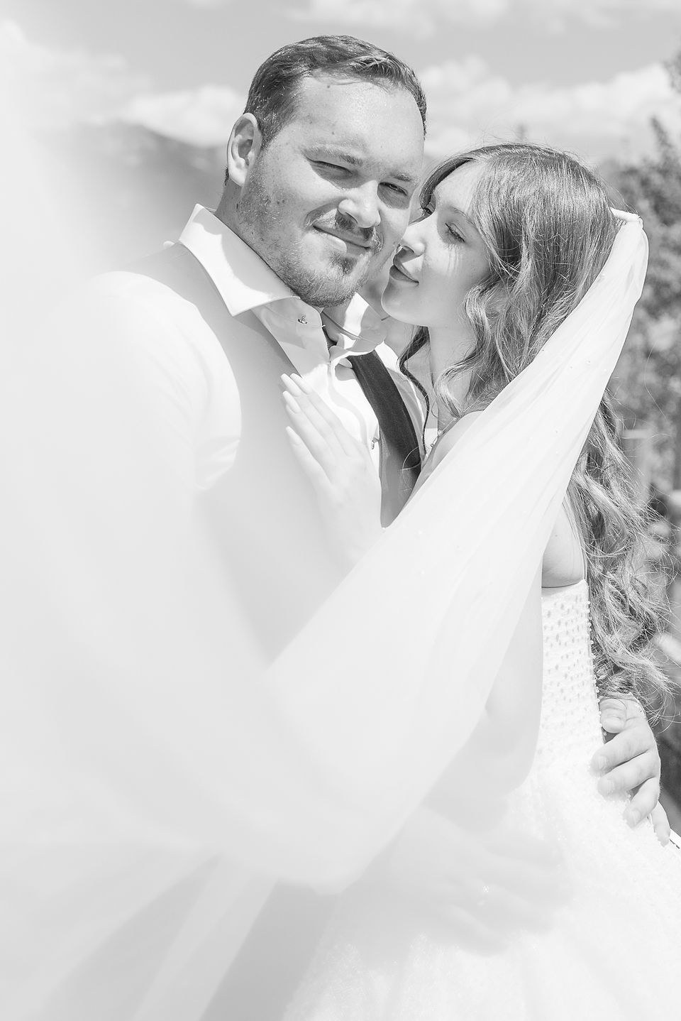 Black and white photo of bride kissing groom with vail blowing in the wind. Captured by Invermere Wedding Photographer