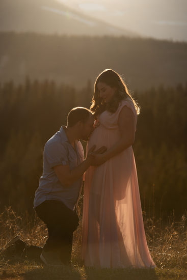 Silhouette of a man kneeling in front of his pregnant wife and lovingly kissing her belly