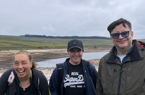 A group of people laughing and smiling at the camera with a scenic backdrop. There is a very low reservoir and some sand in the background.