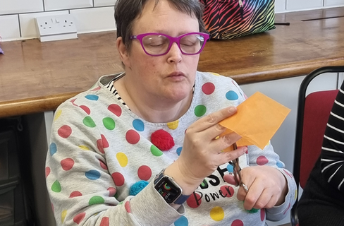 A lady concentrating on cutting a piece of yellow paper.