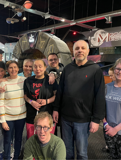 A large mixture of people all stood looking at the camera and smiling. There is a young man crouched down at the front of the group.