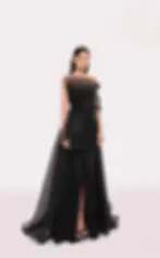A model wearing a sheer black draped couture gown with pleated details and an asymmetrical neckline.