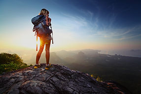 Young lady hiker standing with backpack on top of a mountain and enjoying sunrise_edited.j
