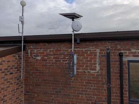 Starlink High Performance dish and wireless bridge mounted on a pole on a red brick wall