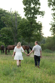 Couple holding hands while leading their horses through a countryside pasture.