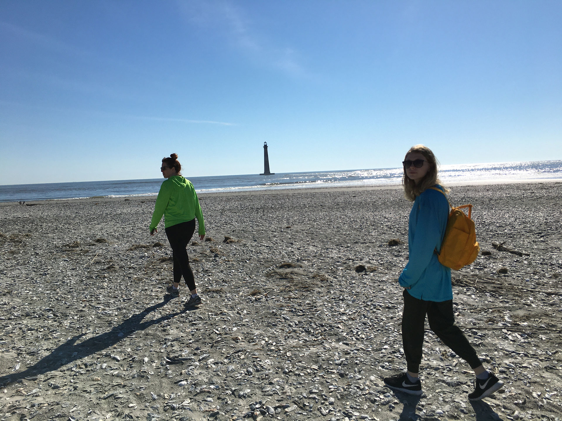 a woman and girl walking across the beach with a lighthouse in the background