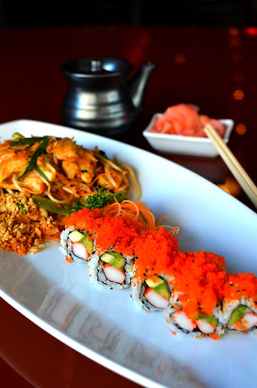 California Rolls Sushi and Chicken Pad Thai Noodle with soy sauce dispencer in the background along with a pair of chopsticks and pickled ginger.