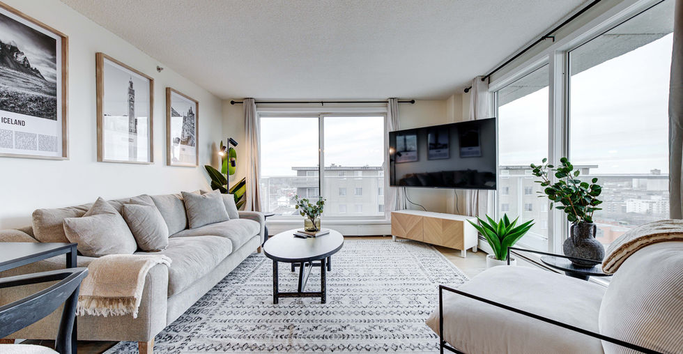Living room featuring a 75 inch smart TV, and comfortable sofa and a desk. This condo is a short-term furnished rental, which is also known as an airbnb. This condo is professionally managed by Squire Hospitality Inc., which is a division of Squire Property Management Inc. in Saskatoon, Saskatchewan.